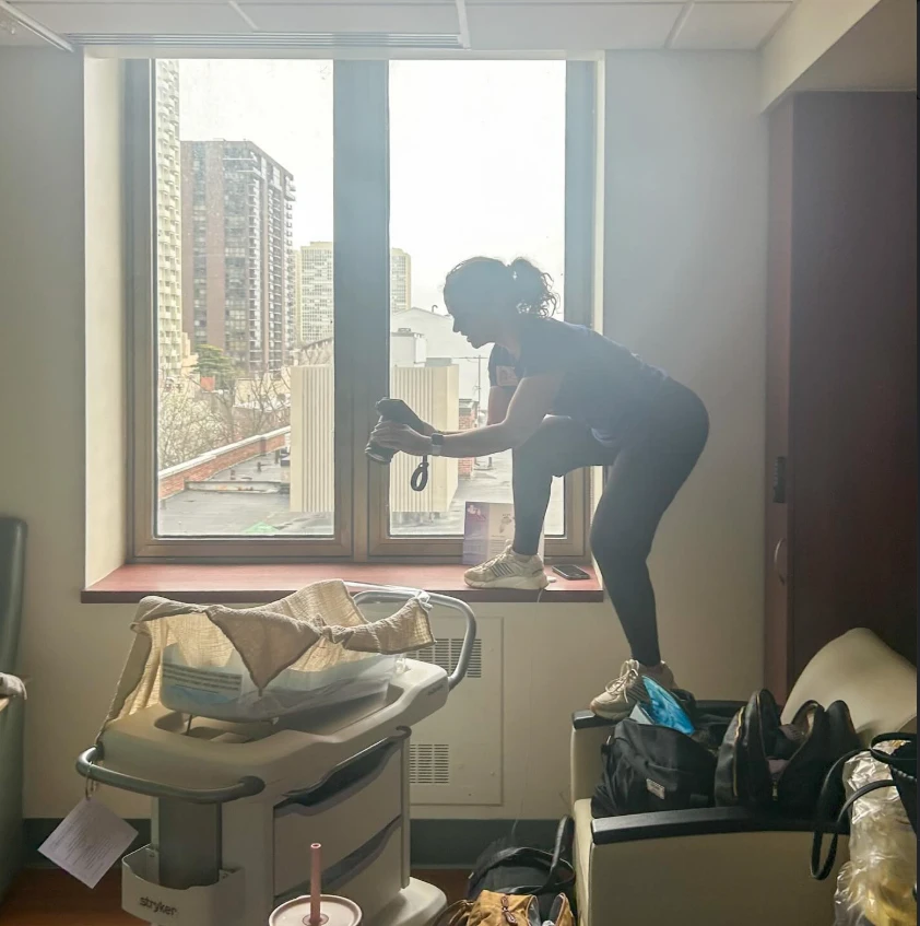 Emily Harvey preparing a birth space at the window of a hospital room, a bassinet waiting nearby